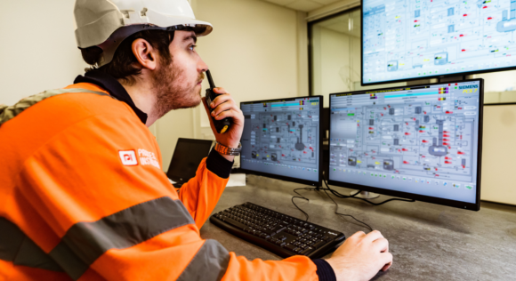 Process Instrument Services engineer working on a factory process map on three computer screens with a walkie talkie in hand