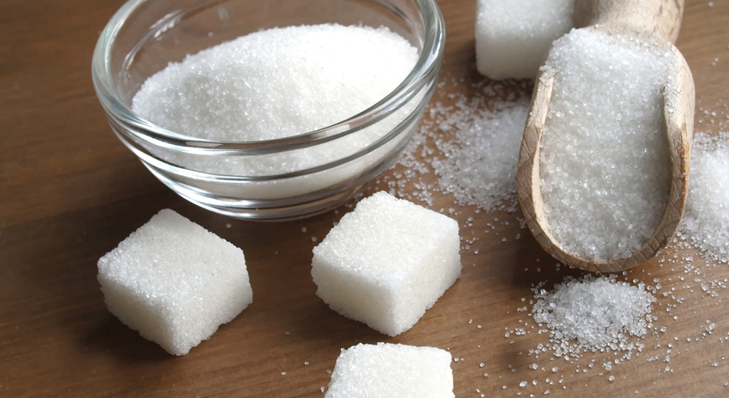 Sugar granules and sugar cubes on a wooden table with a wooden spoon 